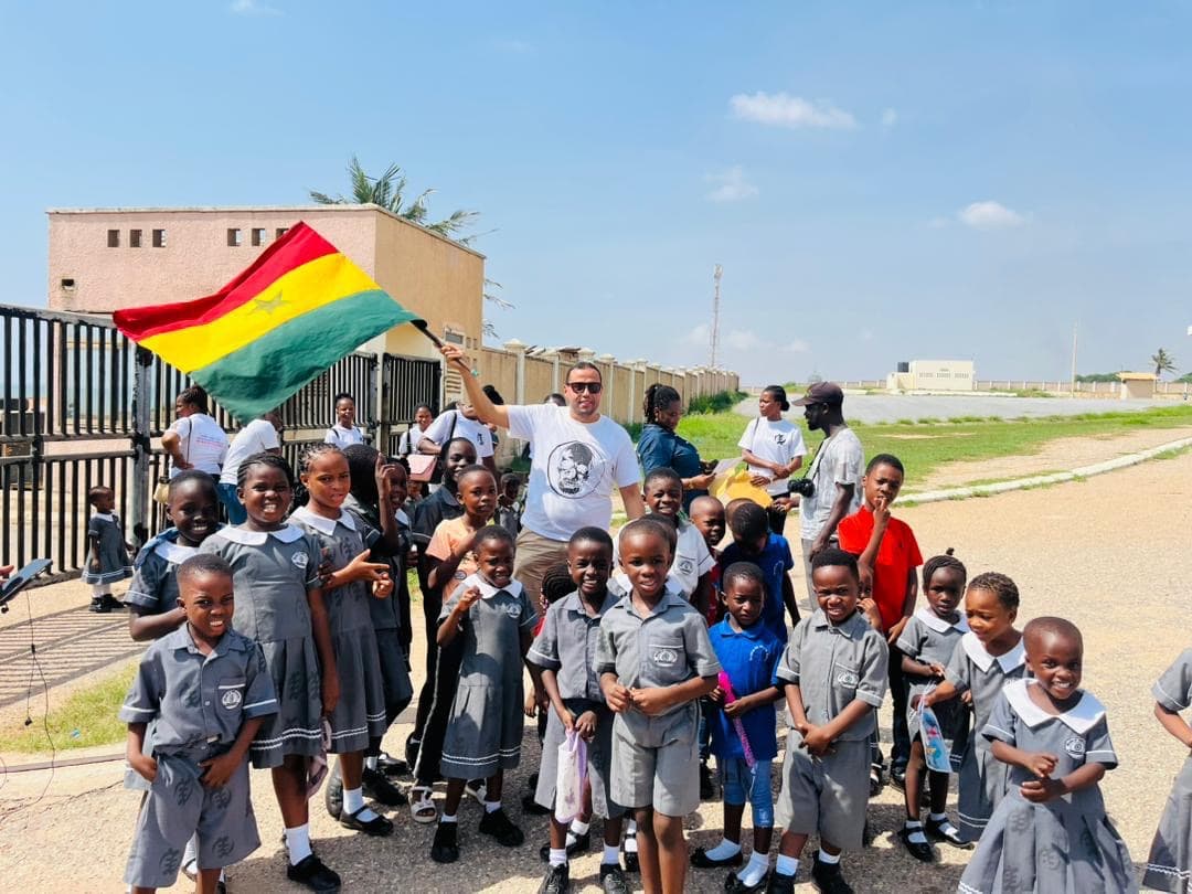 Pupils in grey uniforms at the school gate, with the Ghana flag raised.